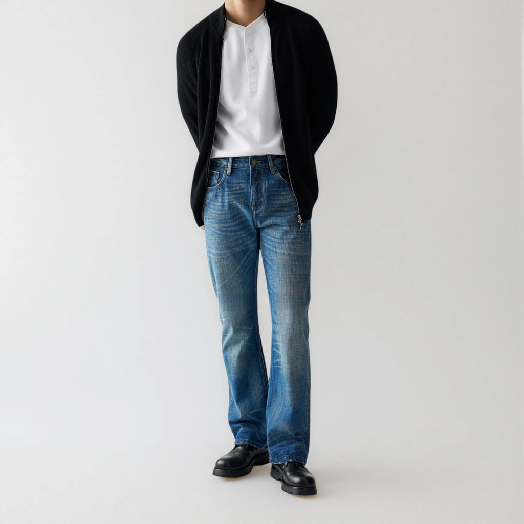 Person wearing a black cardigan, white shirt, blue jeans, and black shoes on a light gray background