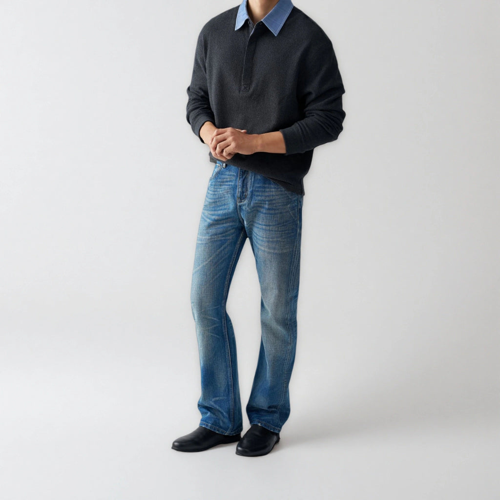 Person wearing a dark sweater, blue shirt, jeans, and black shoes on a white background