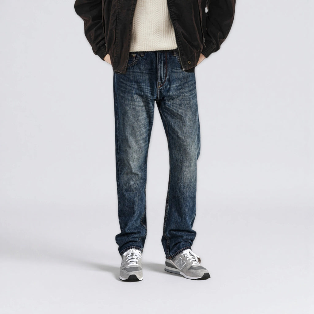 Person wearing blue jeans and a dark jacket on a light gray background