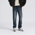 Person wearing blue jeans and a dark jacket on a light gray background