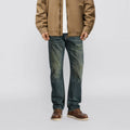 Person wearing a brown jacket, white shirt, blue jeans, and brown shoes on a light gray background