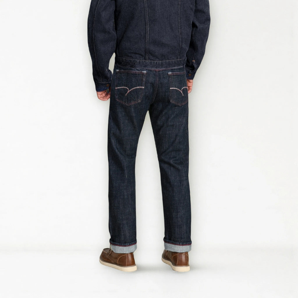 Person wearing dark blue jeans and brown shoes on a white background