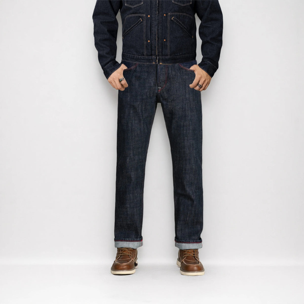 Person wearing a dark denim jacket and jeans with brown shoes on a white background