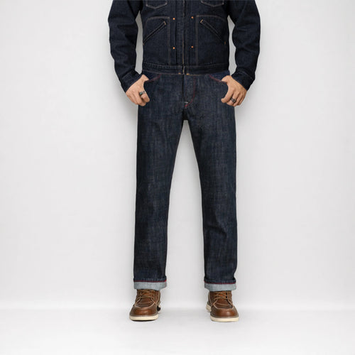 Person wearing a dark denim jacket and jeans with brown shoes on a white background