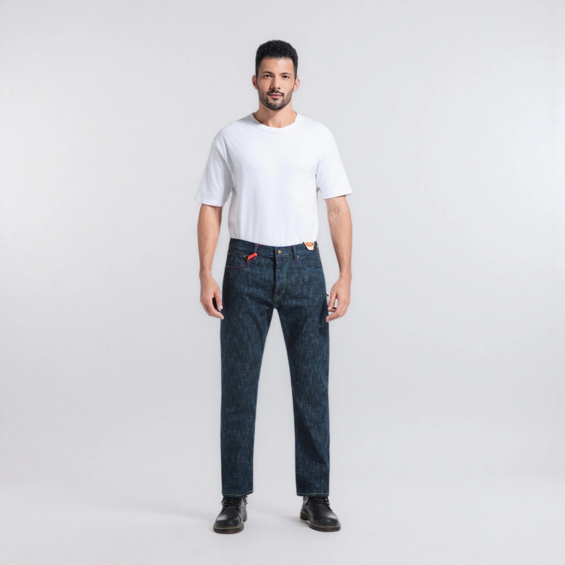 Man wearing a white t-shirt and dark blue jeans on a light gray background