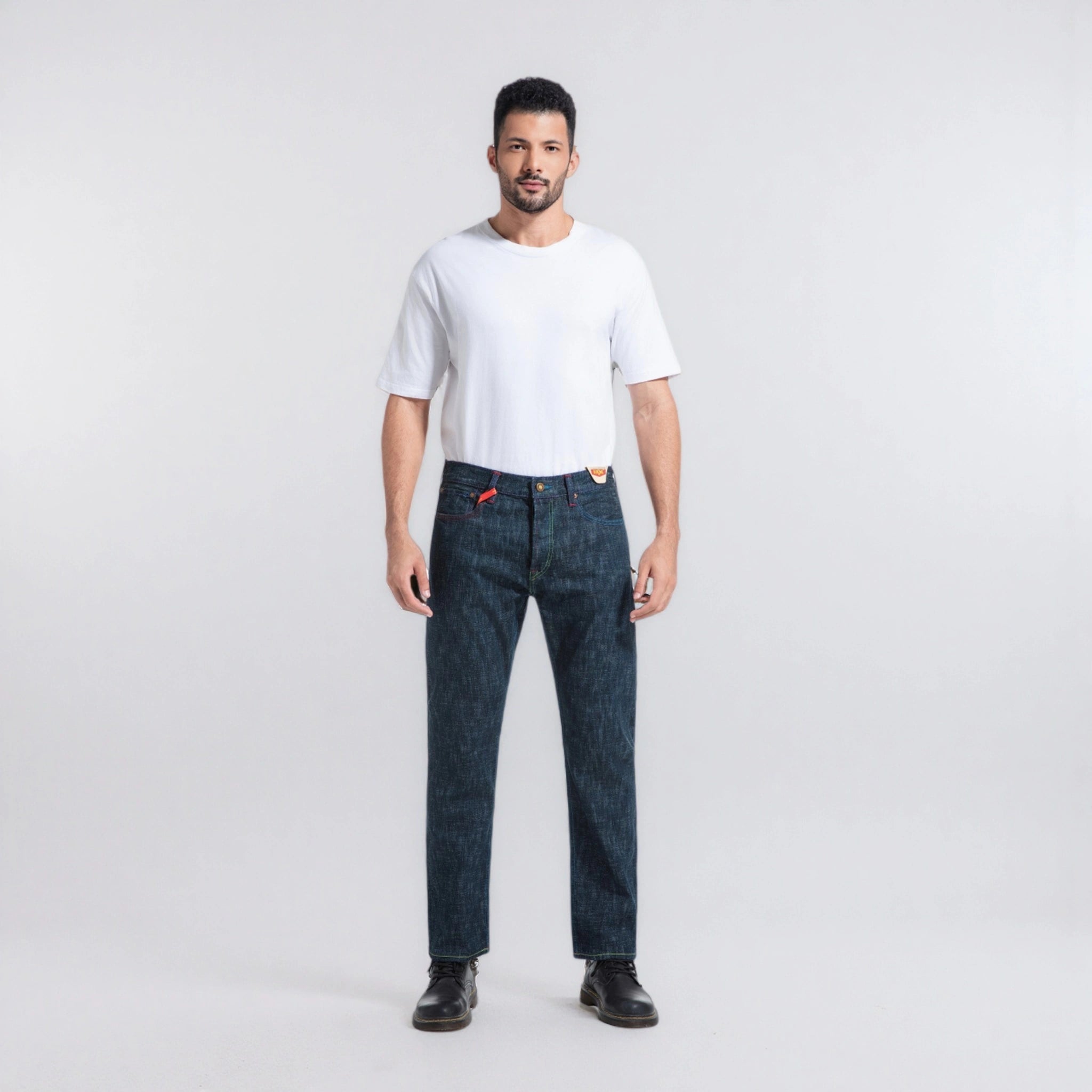 Man wearing a white t-shirt and dark blue jeans on a light gray background
